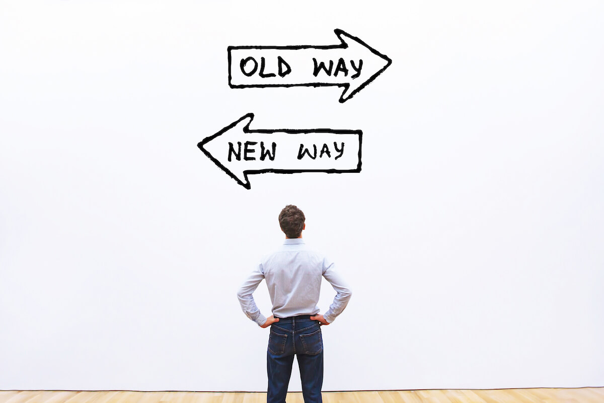 photo of man with opposing signs on the wall that say old way new way