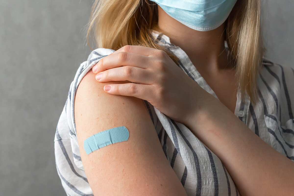 Photo of woman with a bandaid on her upper arm at the site of a vaccination