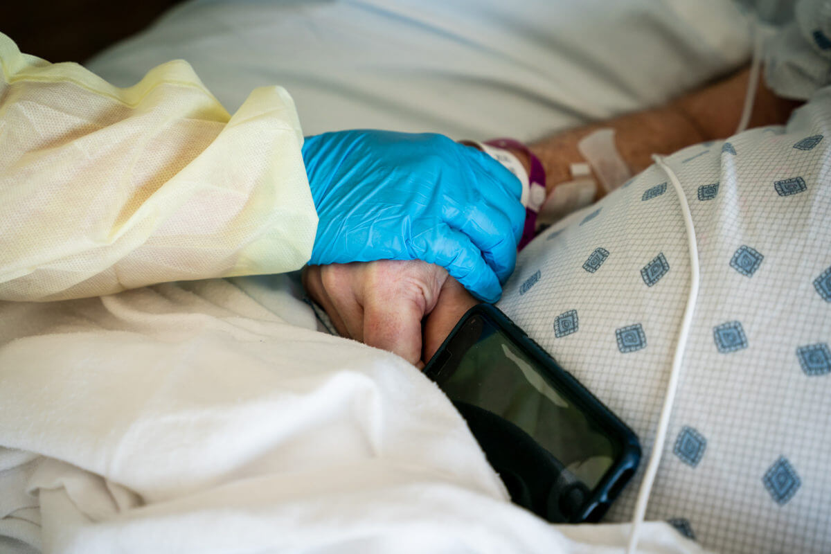 Photo of a caregiver's gloved hand on the hand of a patient at bedside