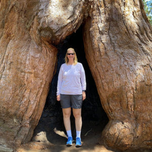 Photo of Joy Plamann standing in an opening to a giant Sequoia Tree
