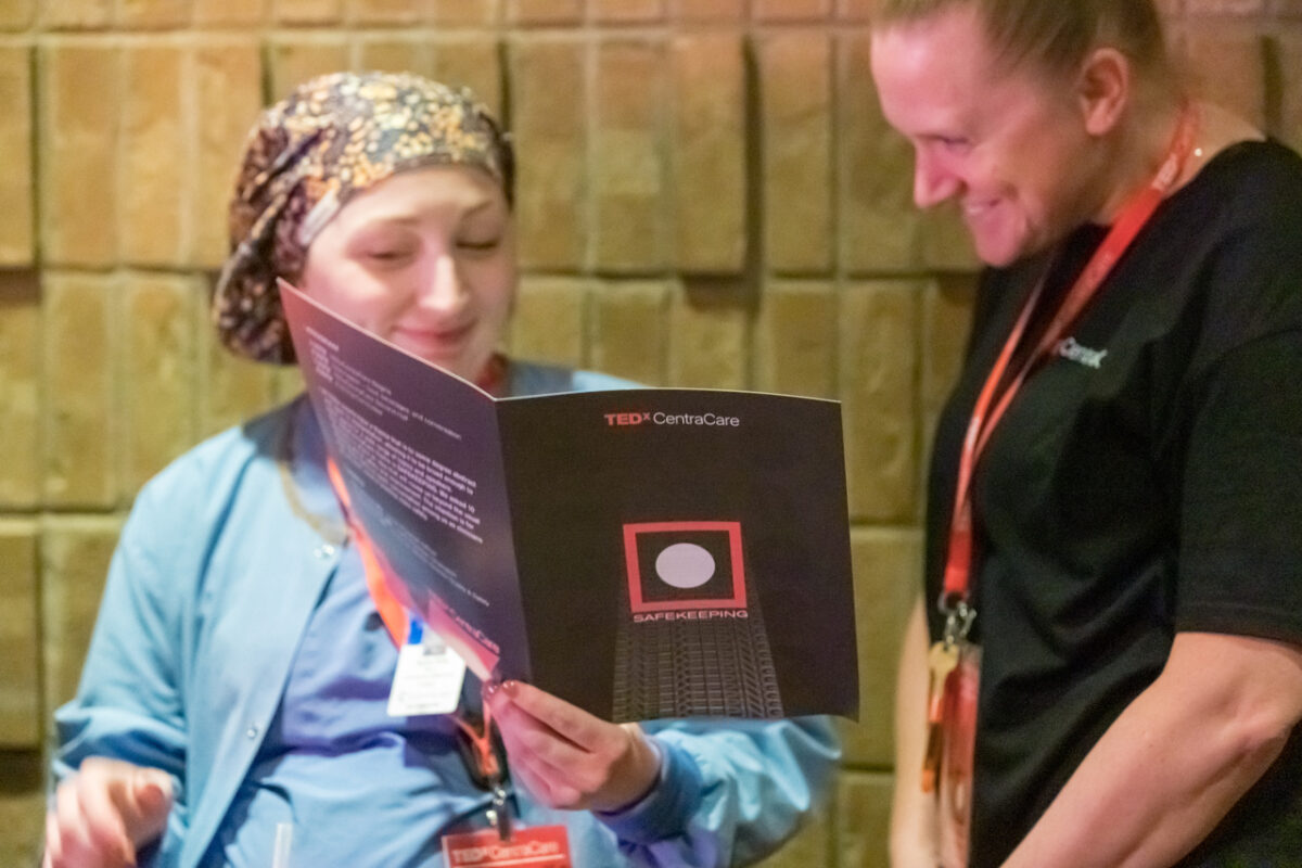 Two attendees share a TEDxCentraCare program