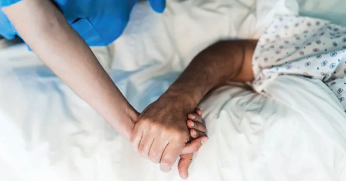 Photo of a caregiver and patient clasping hands on a hospital bed